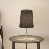 Selmarne Fabric Table Lamp with tapered black cotton shade on a slim satin nickel stem and rectangular base, shown on a round side table in a bedroom setting.