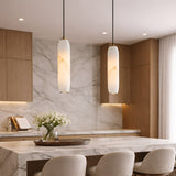 Modern kitchen with light wood cabinets, marble backsplash and countertops, Vireth 1 Light Small Cylinder Alabaster Single Pendant Lights in soft white, beige upholstered chairs, and a vase of white flowers on the island. Natural light comes through sheer curtains.
