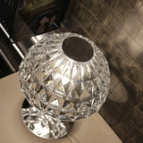 Deco Crystal Table Lamp in chrome, close-up of the faceted crystal dome shade lit from within, showing a chrome stem and base against a leather-textured backdrop.