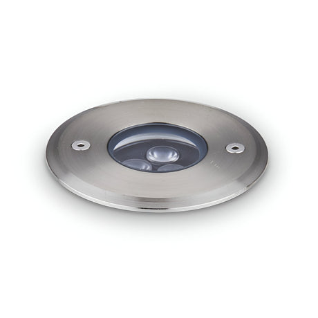 The Emberwave LED Drive Over Outdoor Recessed Ground Light 3W 3000K in grey features a circular design with stainless steel construction and a glass cover showcasing three visible LED bulbs. Engineered for energy efficiency, it boasts an IP67 rating for weather resistance and includes two screw holes for easy installation, making it ideal for lighting pathways or garden areas. Its diameter measures 9cm.