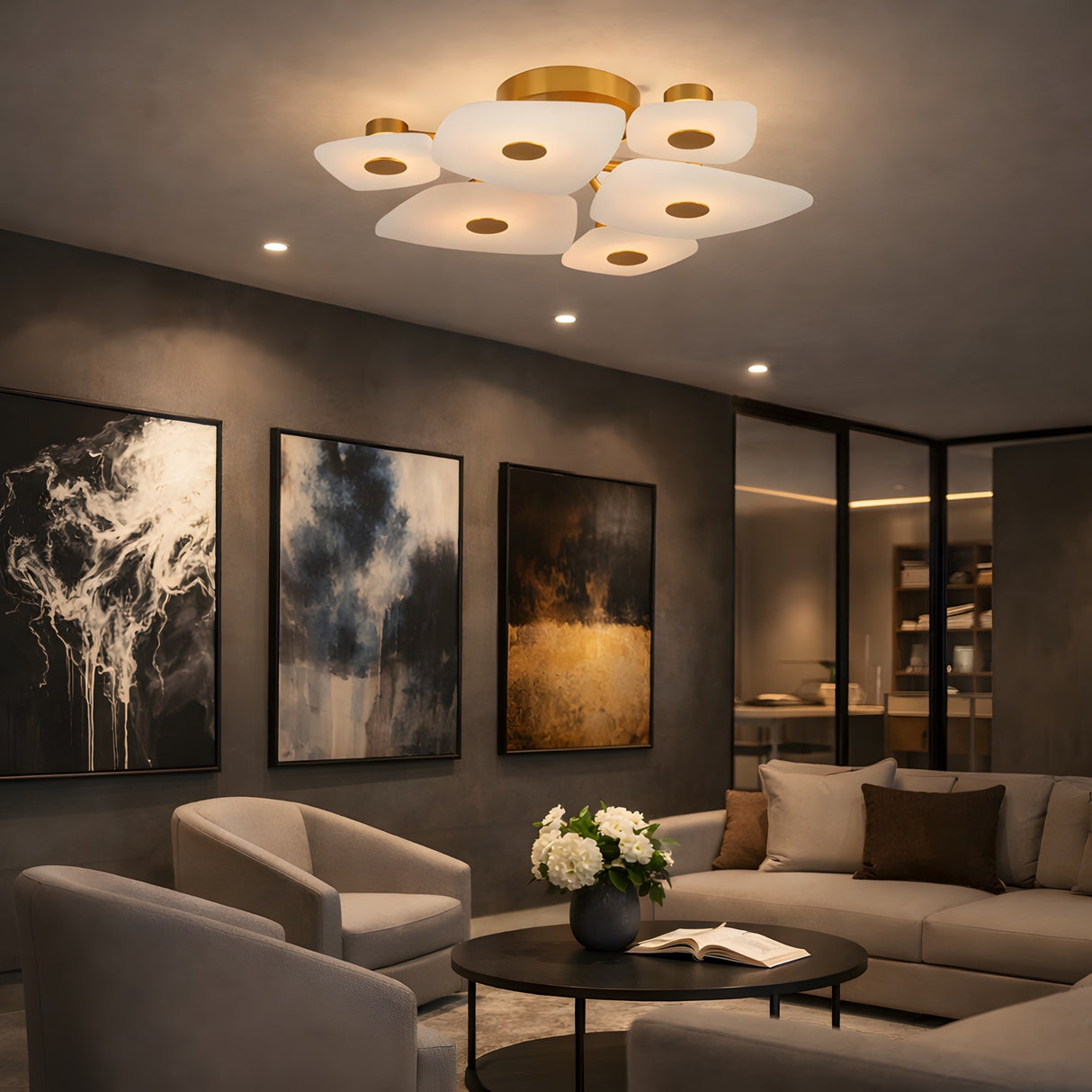 A modern living room with gray chairs, a round coffee table, abstract artwork, and the Calyra LED Small Alabaster Semi-Flush Ceiling Light in Brass & Soft White creates a sophisticated, contemporary vibe.