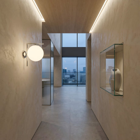 Minimalist hallway with beige walls features the Vetra 1 Light Opal Glass Wall/Semi-Flush Ceiling Light in grey above, a glass shelf with a white vase, and large windows at the end revealing a cloudy cityscape view.