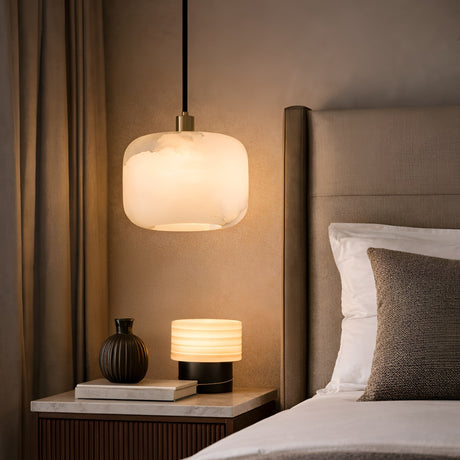 A cozy bedroom featuring a beige upholstered bed, tidy pillows, a wooden nightstand with a round ribbed lamp and dark vase, and the Calvex 1 Light Small Rounded Alabaster Single Pendant Light in Soft White softly glowing above.