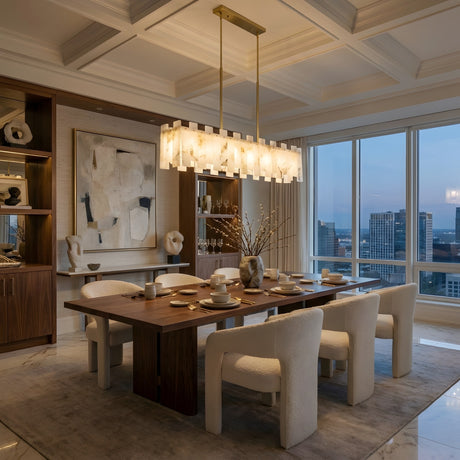 Modern dining room with a wooden table, six white upholstered chairs, abstract wall art, sculptural decor, floor-to-ceiling windows framing a city skyline at dusk, and the Lunaro Linear Panel Alabaster Chandelier in Brushed Brass & Soft White.