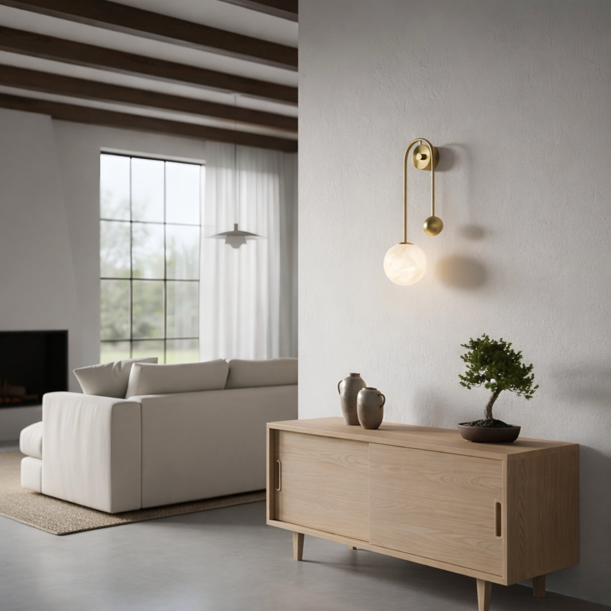 A minimalist living room with a light wood sideboard, bonsai tree, ceramic vase, Risa 1 Light Arched Drop Alabaster Wall Light in soft white & brass, cream sofa, large windows, white walls, and exposed wooden ceiling beams.