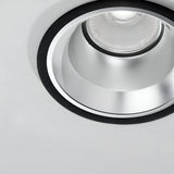 Close-up of the Zeal Outdoor LED Recessed Downlight - 28W, 3000K, Black, featuring an IP54-rated metallic frame. This light fixture is embedded in a white ceiling and turned off, showcasing a circular reflective surface surrounding the bulb area.