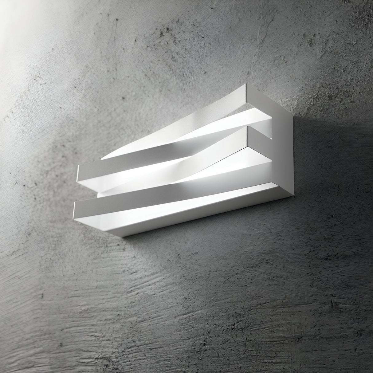 The Ember LED Wall Light 17W 3000K in White features a sleek geometric design with overlapping rectangular layers, providing a modern, dynamic appearance. It emits warm, consistent light against a textured gray wall while ensuring energy efficiency for eco-conscious style enthusiasts.