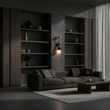 A modern living room with a dark grey sofa, neutral cushions, wood shelves, a coffee table, and sheer curtains is beautifully accented by the Zeal 1 Light Vertical Orb Alabaster Wall Light in soft white, black, and brass.