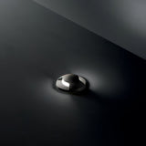 Against a dark background, the Solarium Outdoor Drive Over Recessed Light Two-Sided 3000K in Black casts a soft, ambient glow with its dimly lit brilliance. Shadows accentuate its sleek, metallic surface and elegant design. This luminaire mirrors the high-performance resin typical of outdoor fixtures, underscoring both durability and style.