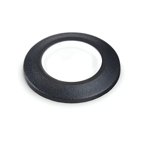 The Solarium Outdoor Drive Over Recessed Light 4000K in black, which appears as a circular object with a transparent center similar to a glass or lens encased in a black frame, is showcased on a white background. This light boasts an IP67 rating, guaranteeing its durability and protection against harsh outdoor conditions.