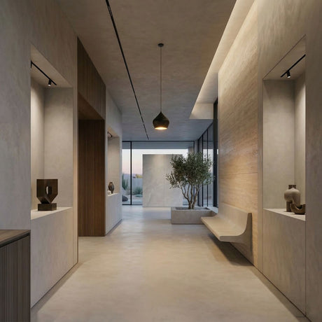 A minimalist hallway with smooth beige walls, built-in benches, sculptures on display, a potted tree by large glass windows, and Funk Stout Small Pendant Light - Black overhead for a serene, modern atmosphere.