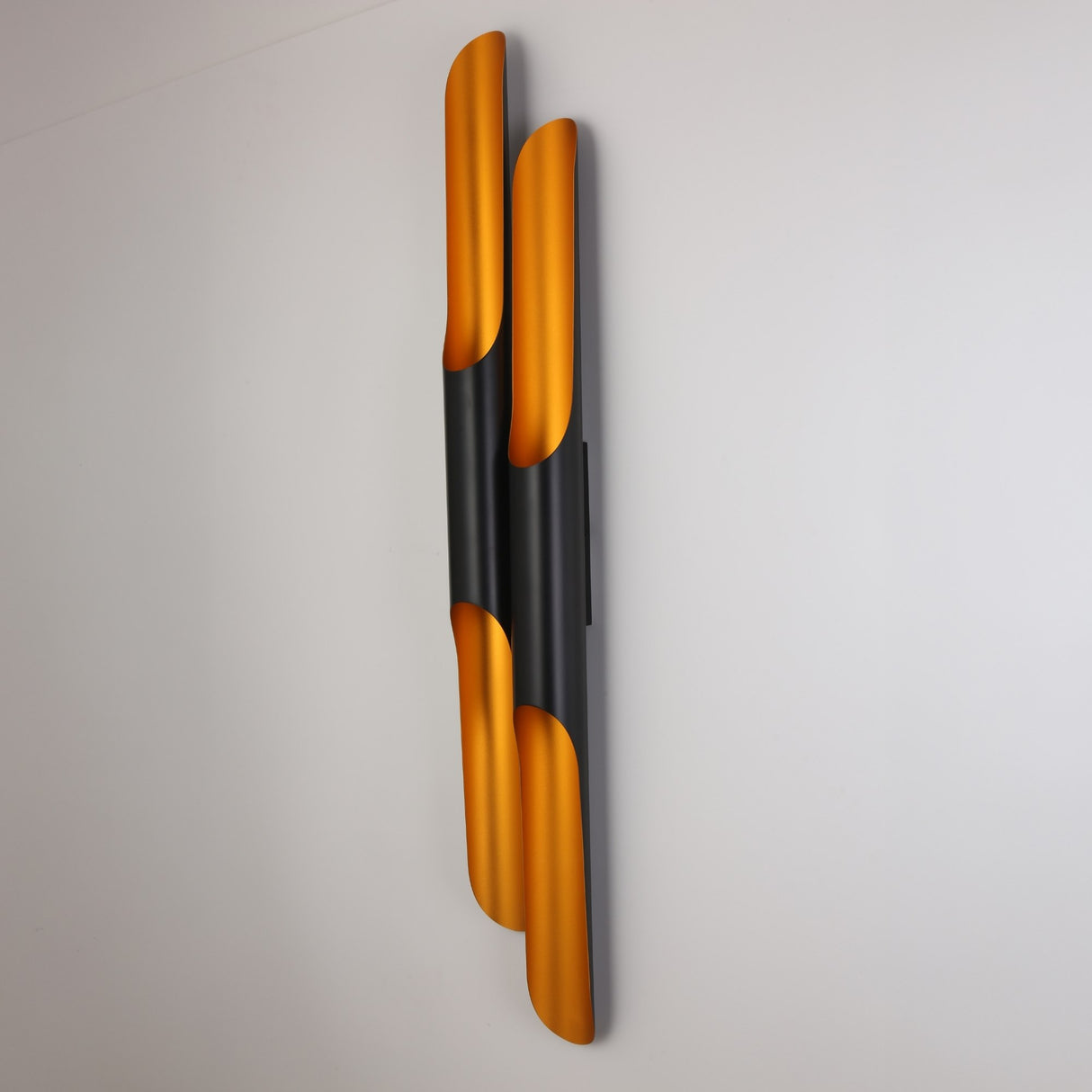 The Stealth 4 Light Wall Light in brass and black features sleek, vertical curved tubes with a matte black finish and gold interior, creating a modern look and casting warm light against white walls.