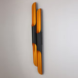 The Stealth 4 Light Wall Light in brass and black features sleek, vertical curved tubes with a matte black finish and gold interior, creating a modern look and casting warm light against white walls.