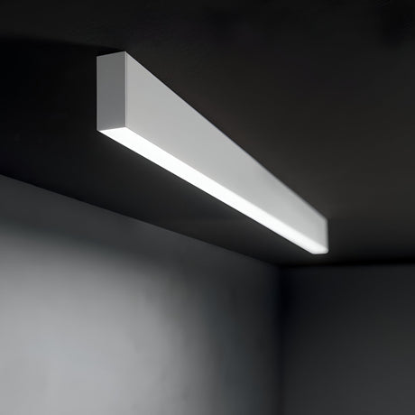 The Ignitia-2 LED Suspension Light 36W 4000K - White, a sleek rectangular fixture, is mounted on a dark ceiling, casting a soft glow throughout the space. Its energy-efficient design perfectly complements contemporary interiors with its minimalist charm.