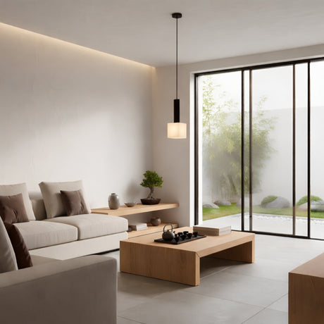 A modern minimalist living room with white walls, light wood furniture, a low coffee table, beige sofas with brown cushions, and the Norevia 1 Light Cube Alabaster Single Pendant Light in soft white & matte black overhead. Glass doors lead to a small garden.