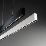 Two sleek, rectangular pendant lights—one in black and the other featuring the Celine LED Linear Suspension 30W 4000K in white—hang parallel from thin cords against a gray gradient background. These fixtures incorporate small, recessed bulbs along their undersides for excellent glare control.