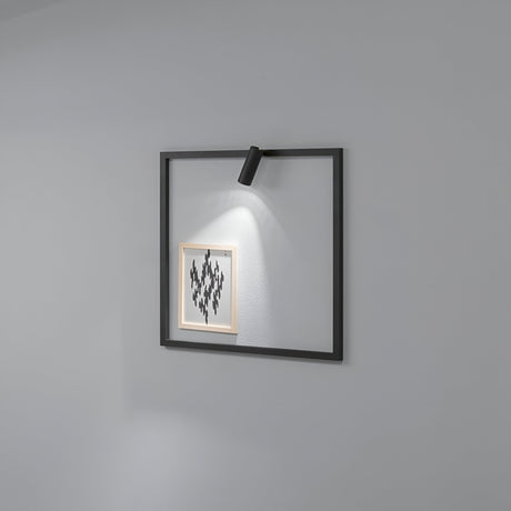 A minimalist frame featuring a small geometric pattern is mounted on a gray wall, subtly illuminated by the Glimmer LED Square Wall Light 5W 3000K in black. The LED light enhances the artwork with gentle shadows, and its square shape and simple, modern design make it an ideal contemporary lighting solution for any space.