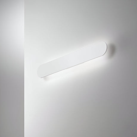 The Luster Wall Light 30W 3000K - White, 60cm features a modern, minimalist design that uses LED technology to cast a soft glow on a light gray wall. Its elongated, rounded rectangular shape and sleek design deliver a subtle yet elegant indirect lighting effect.