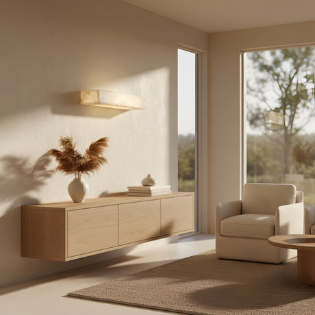 A minimalist living room with light wood furniture, a white armchair, a round table, and large windows showcases the Caelith LED Large Alabaster Shelf With Light – Soft White for an elegant illuminated display.