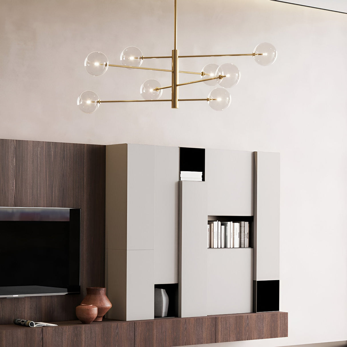A modern living room is adorned with the Solarae 8 Light Suspension in brass, which boasts multiple glass globes and transparent diffusers. A minimalist entertainment center with geometric shapes holds a TV and books, while various decorative vases are arranged on the wooden shelf. The walls are painted a soft beige.