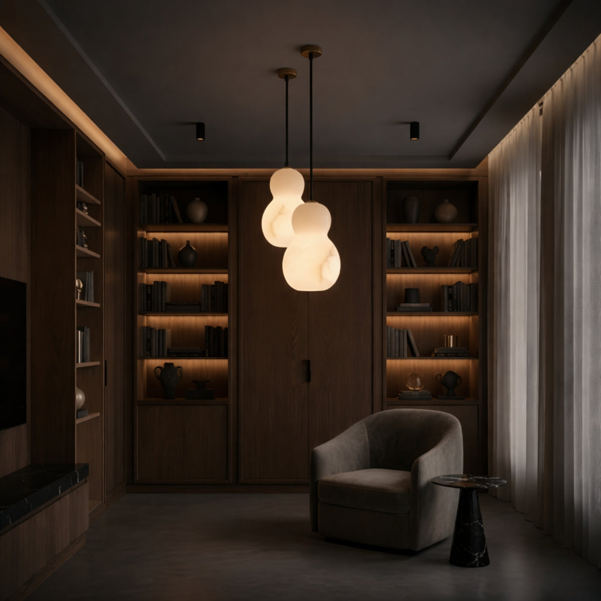 A cozy, modern reading nook features a curved armchair, round side table, and the Orlune LED Sculpted Pear Alabaster Single Pendant Light - Soft White. Built-in wooden shelves with books and decor are softly illuminated by warm lighting.