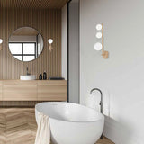 Libra Glass Globe Wall Light with three round glass globe shades on a wood-tone stem, mounted above a bathtub in a modern bathroom.