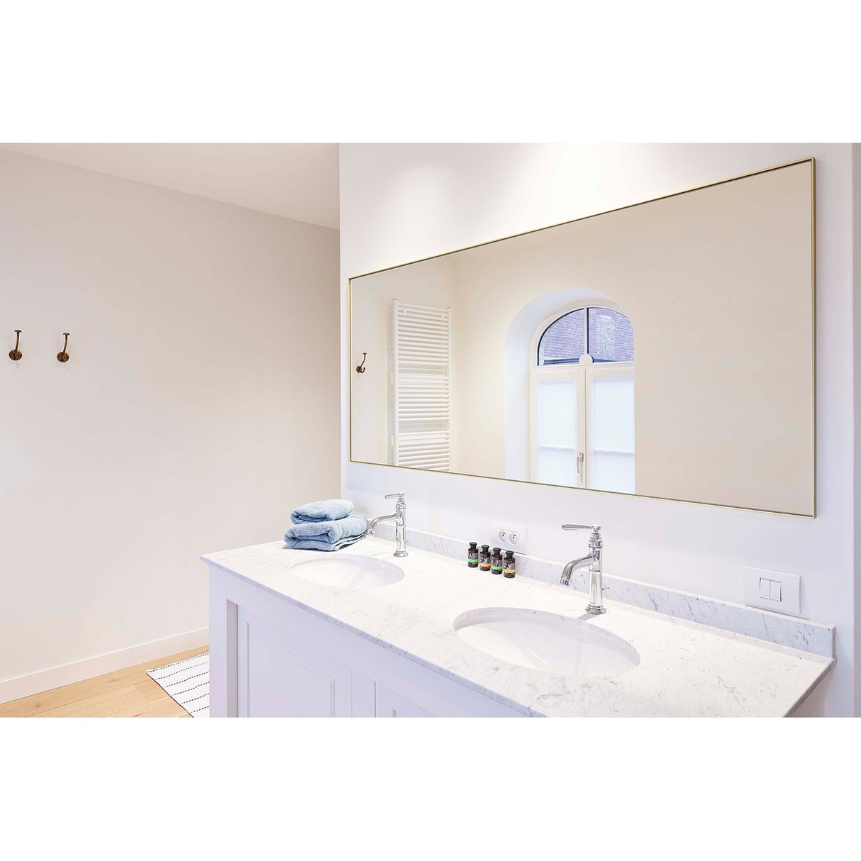 Lucka Gold Framed Full Length Mirror mounted above a bathroom double vanity, its slim gold metal rectangular frame and clear glass reflecting an arched window.