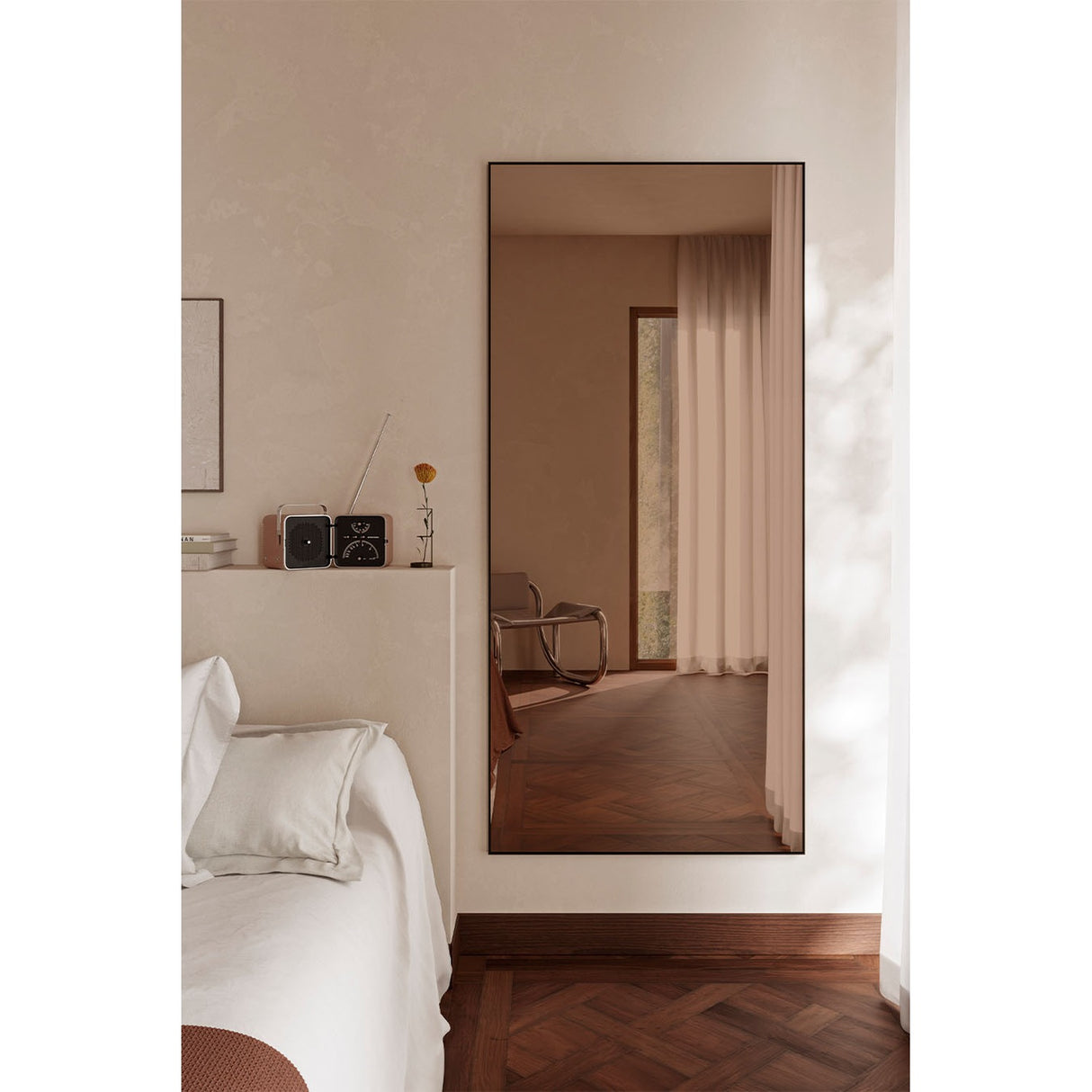 Lucka Bronze Tinted Full Length Mirror 175cm in a slim black metal frame, mounted on a bedroom wall, reflecting a doorway with sheer curtains and herringbone wood flooring.