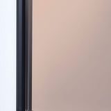 Close-up of the Lucka rectangular wall mirror's edge, showing the slim black metal frame beside the bronze-tinted glass reflecting a warm, muted tone.