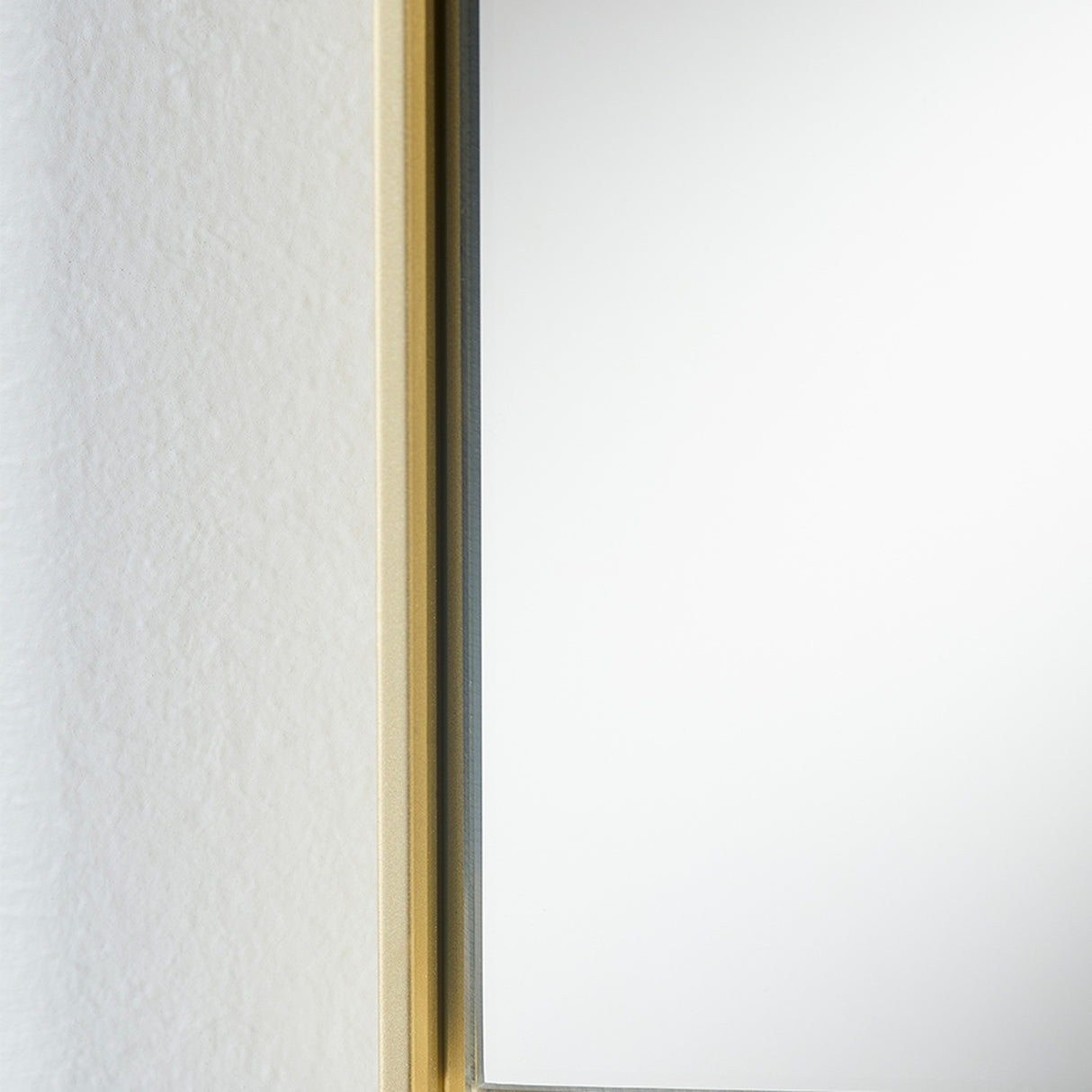 Close-up of the Lucka Gold Slim Framed Full Length Mirror, showing the narrow gold metal frame edge against a textured white wall with flush mirror glass.