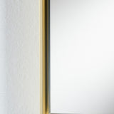 Close-up of the Lucka Gold Slim Framed Full Length Mirror, showing the narrow gold metal frame edge against a textured white wall with flush mirror glass.
