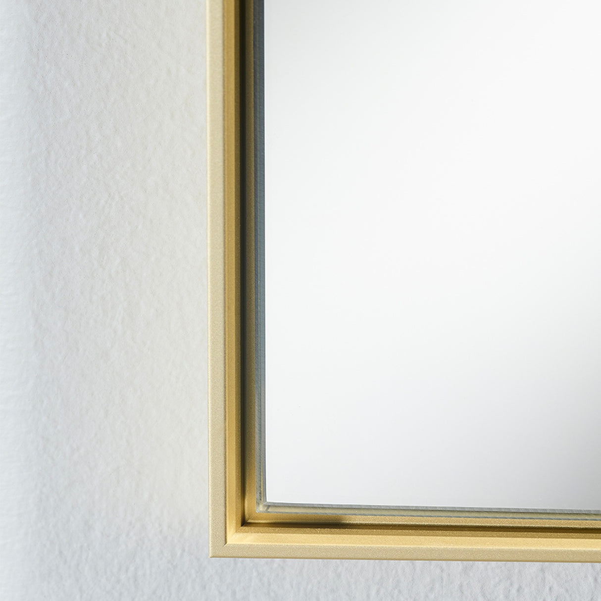 Close-up of the Lucka Gold Framed Full Length Mirror's corner, showing a slim gold metal frame with clear glass flush to the front, against a plain white wall.