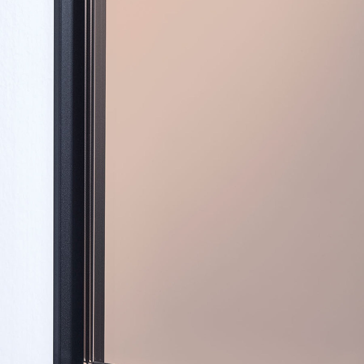 Close-up of the Lucka Bronze Tinted Full Length Mirror, showing the slim black metal frame edge against the bronze-tinted glass and white wall corner.