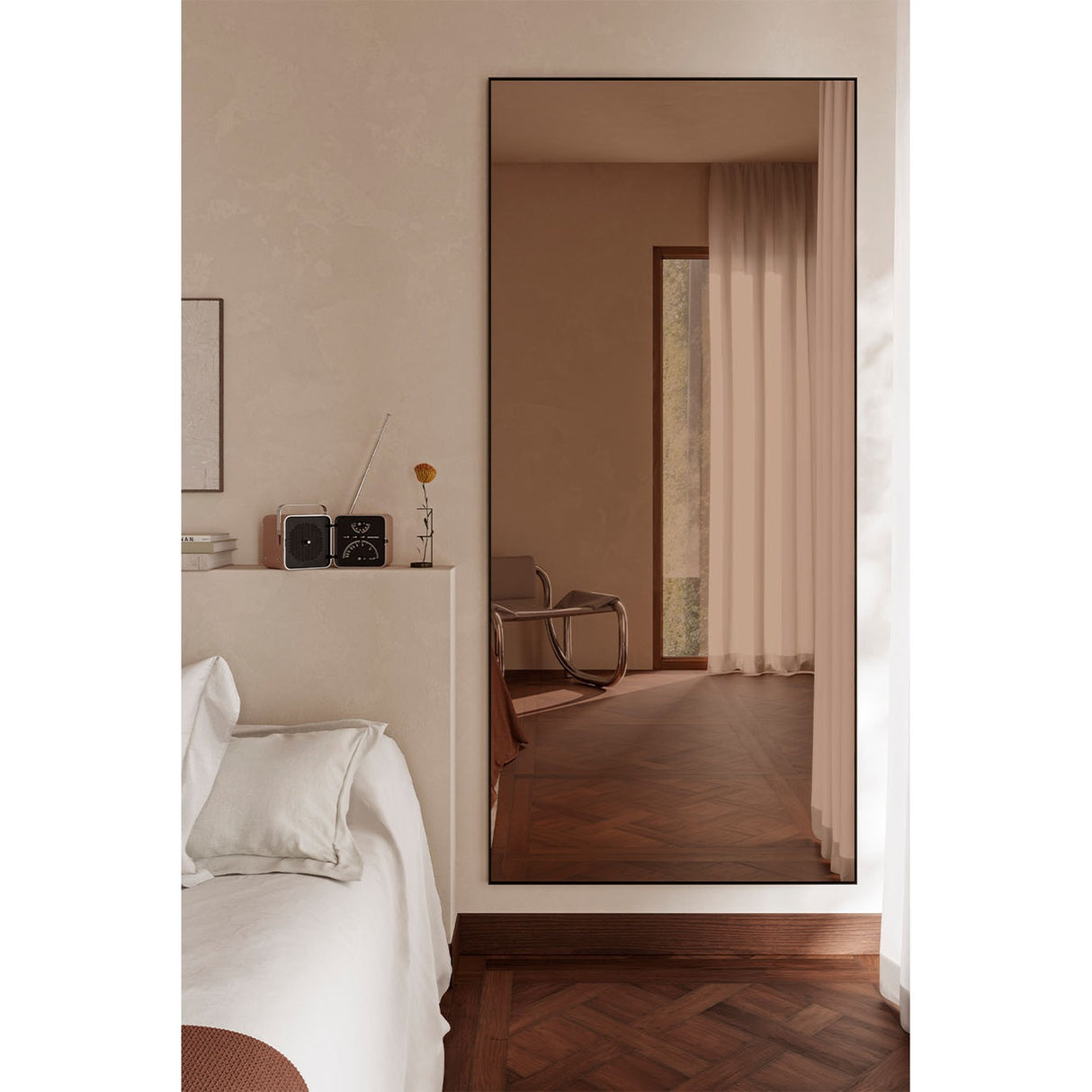 Lucka Bronze Tinted Full Length Mirror 200cm in a black metal frame, leaning against a bedroom wall and reflecting a warm-toned interior with curtains and herringbone wood flooring.