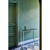 Mesa White console table with slim white metal frame and dark mirrored glass top, styled in a green hallway beside a panelled door with a small glass vase on top.