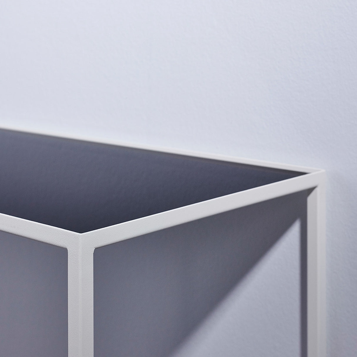 Close-up of the Mesa White console table's corner joint, showing the slim white metal frame and reversible mirrored glass top in dark grey, against a plain light background.