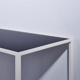 Close-up of the Mesa White console table's corner joint, showing the slim white metal frame and reversible mirrored glass top in dark grey, against a plain light background.