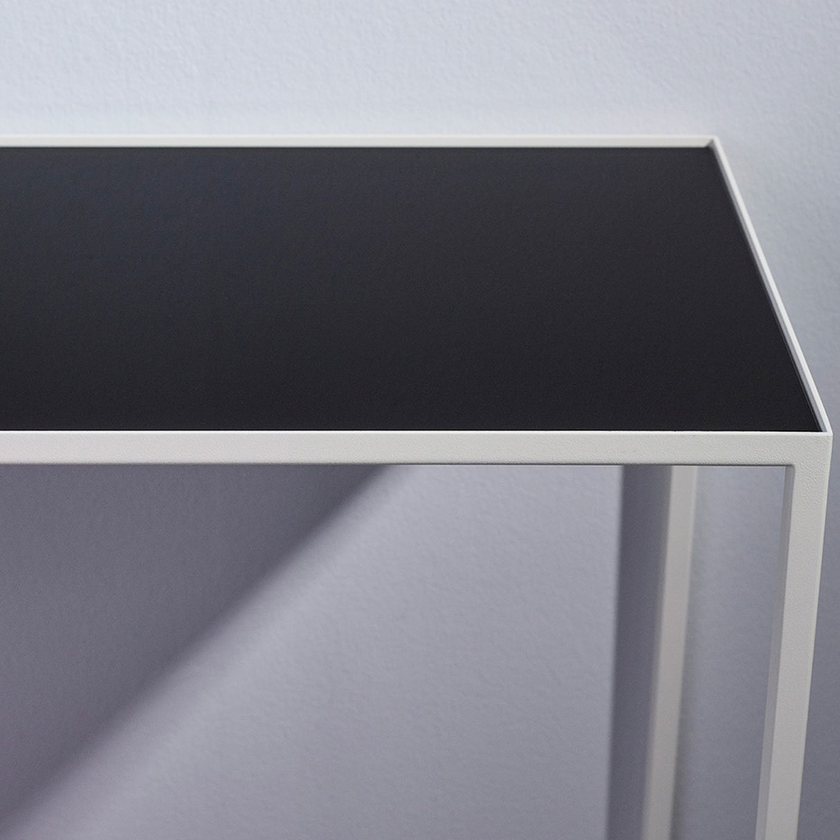 Close-up of the Mesa White console table showing the black reversible mirrored glass top and slim white metal frame with tapered legs against a plain background.