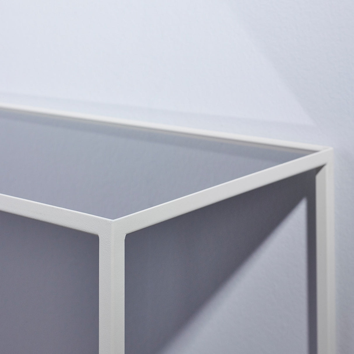 Close-up of the Mesa White console table's corner, showing the slim white metal frame and grey mirrored glass top and side panel.