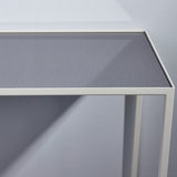 Close-up of the Mesa White console table's corner, showing the slim white metal frame and grey-tinted mirrored glass top against a light grey background.