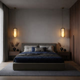 A modern bedroom with a large bed, dark blue bedding, gray headboard, and wooden nightstands features globe lamps and a Vale 1 Light Faceted Alabaster Single Pendant Light in Soft White. Neutral tones and soft lighting add coziness over the wood floor and gray rug.