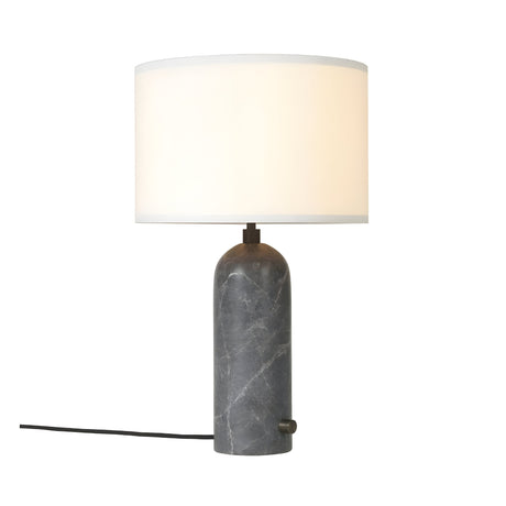 The Arvello 1 Light Minimal Marble Table Lamp features a cylindrical dark grey marble base, a large round white lampshade, and a visible black power cord extending to the left.