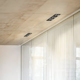 A modern interior with a ceiling featuring Voltis Square Triple Frame 206mm lights in a sleek black finish. The room's large glass walls, adorned with sheer curtains, allow natural light to filter through, complementing the minimalist design of the ceiling and walls.
