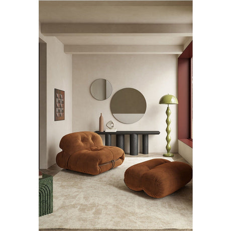 Round frameless wall mirror with plain and textured glass sections divided by a cord motif, shown above a dark console table in a living room.