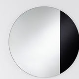 Cord Black Half Tinted Round Wall Mirror 58cm, a frameless circular mirror split vertically into clear glass and black tinted glass, mounted on a plain light wall.