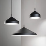 A trio of Elysian 1 Light Pendants in black, each with a sleek conical design and measuring 21cm, are suspended at varying heights against a minimalist white backdrop. These illuminated lamps cast gentle light and shadows on the wall, making them an ideal addition to minimalist interiors.