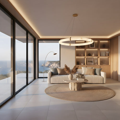 Modern living room with large windows overlooking the ocean, neutral sofa, round wooden coffee table, circular rug, built-in shelves, and the Aureon LED Small Alabaster Circular Suspension Light – Soft White. Soft natural light fills the space.