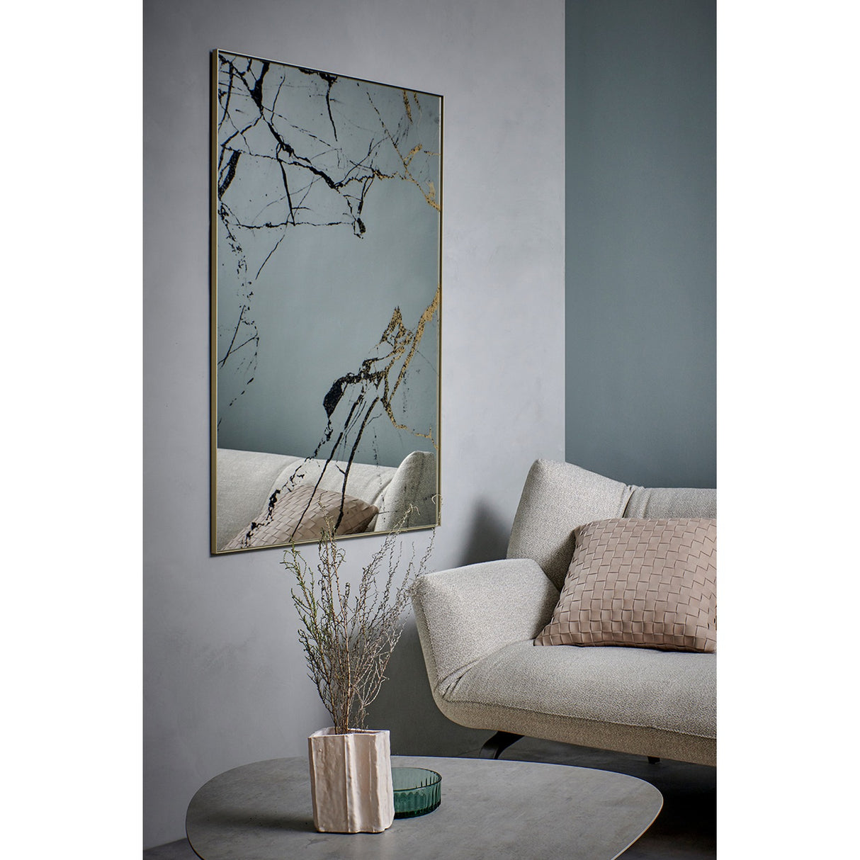 Rectangular wall mirror with gold frame, marble-effect black and bronze veining on the glass, hung in a living room above a beige sofa with cushions.