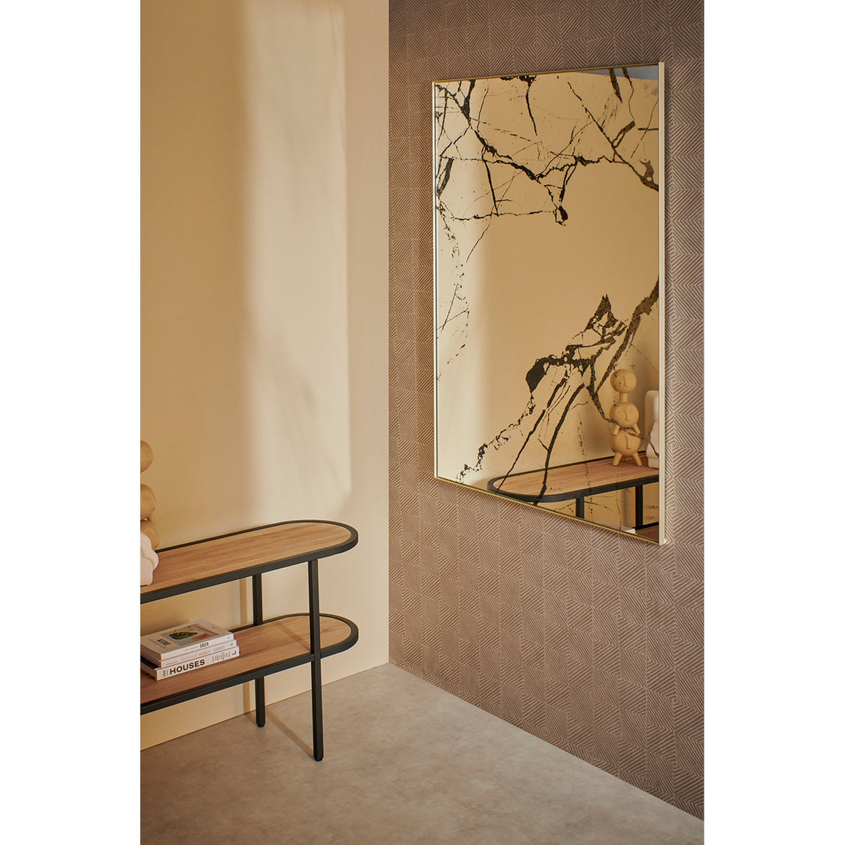 Rectangular wall mirror with gold frame in a hallway, glass surface printed with black marble veining, mounted above a wooden console table.