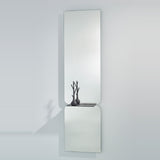 Taille full length hall mirror, 180cm, frameless rectangular glass in two panes with rounded join and black metal shelf, shown on a plain light grey wall.